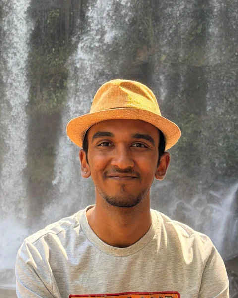 Rithin Nagaraj, smiling, in a straw fedora in front of a waterfall